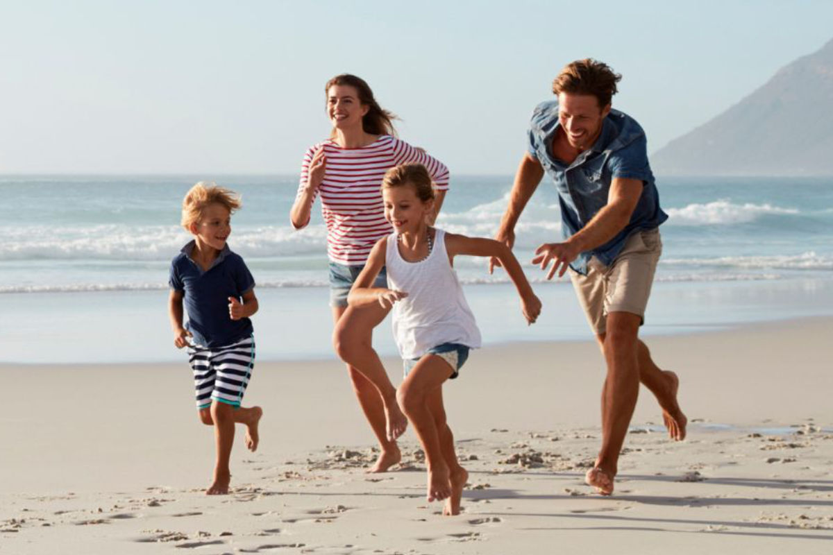 A foster family running together on a bright and sunny beach